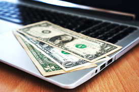 Dollar bills spread out on open laptop