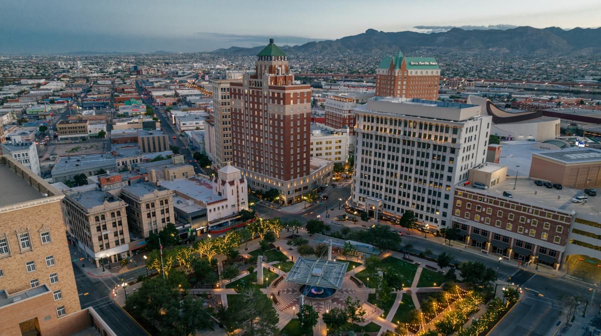 The UTEP campus and El Paso at sunset, seen from a hillside, with mountains on the horizon.