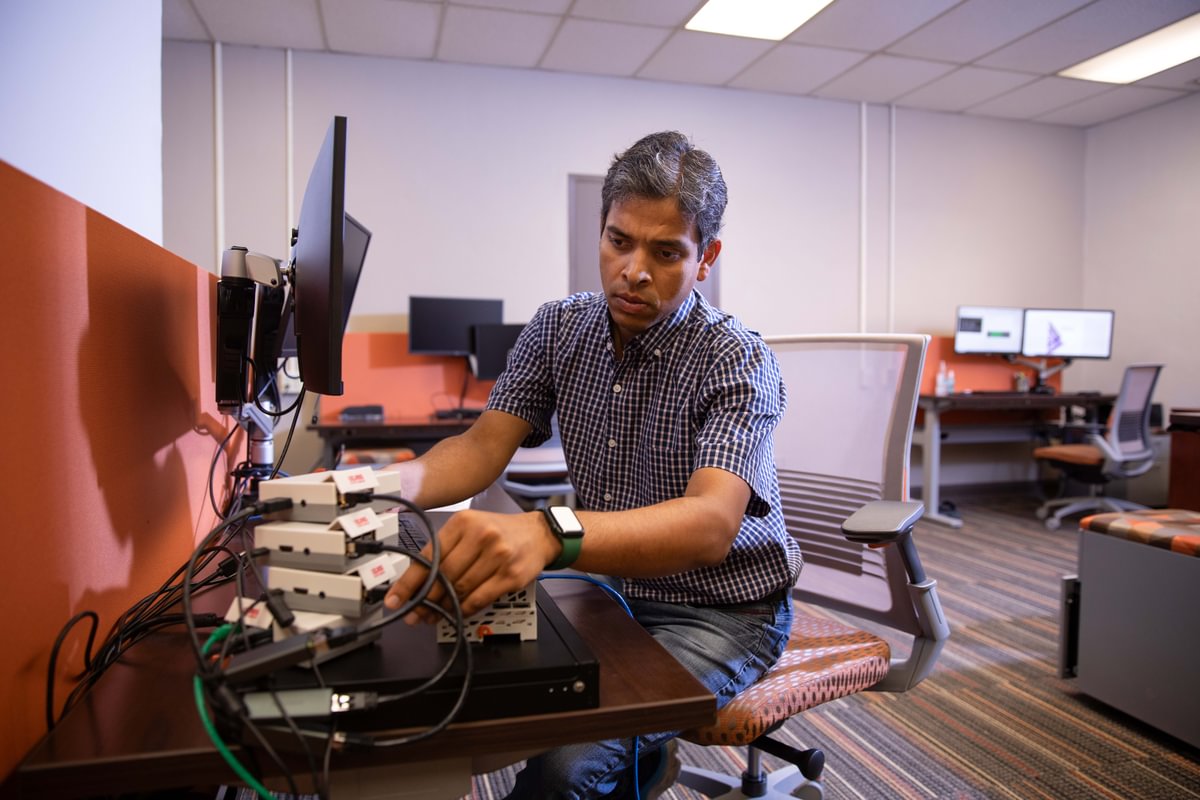 A researcher smiles while working at an open rack in a server room.