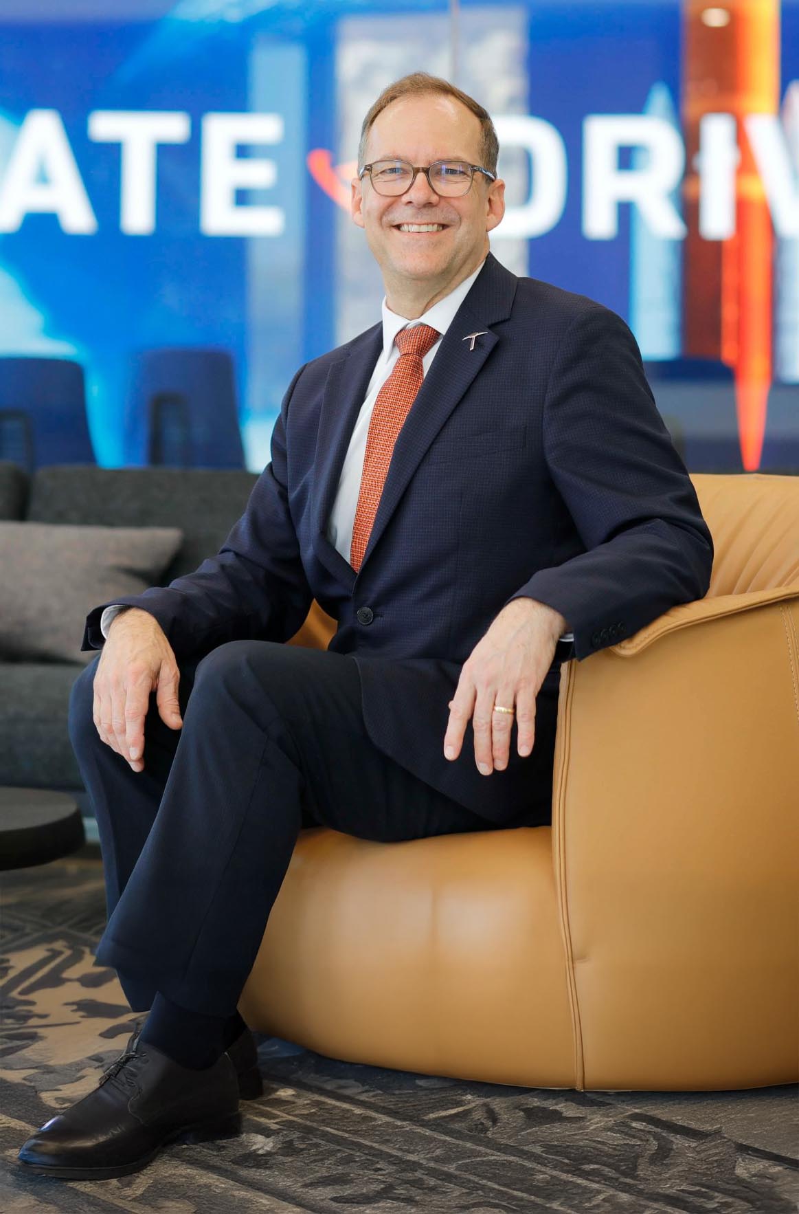Kenith Meissner, Dean of the Miguel A. Loya College of Engineering wearing a dark suit and orange tie seated in a tan leather chair in a modern office setting.