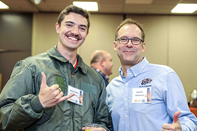 Two people posing together at an indoor networking event while making hand gestures toward the camera.