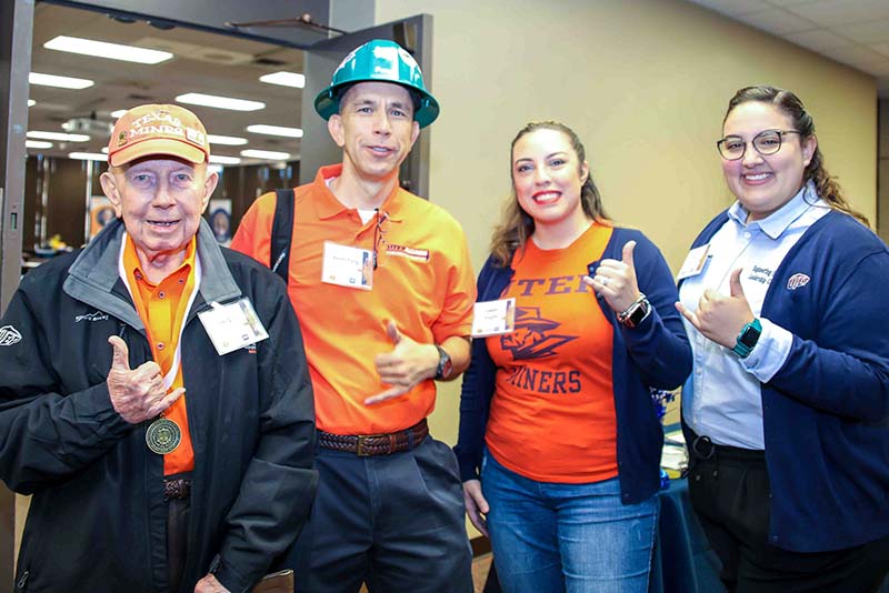 Four people posing together at the Loya Engineering 2022 Homecoming breakfast while making hand gestures toward the camera.