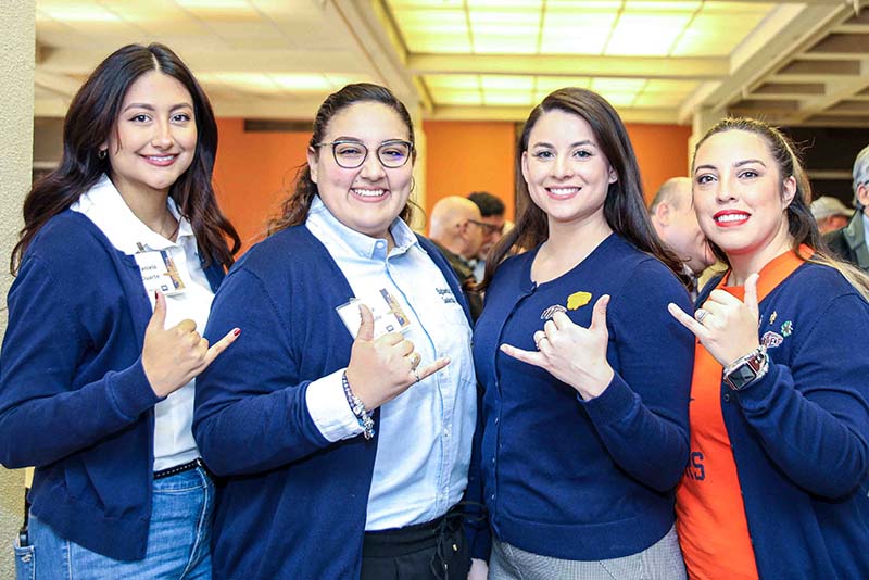 Four people posing together at an indoor event while making hand gestures toward the camera.