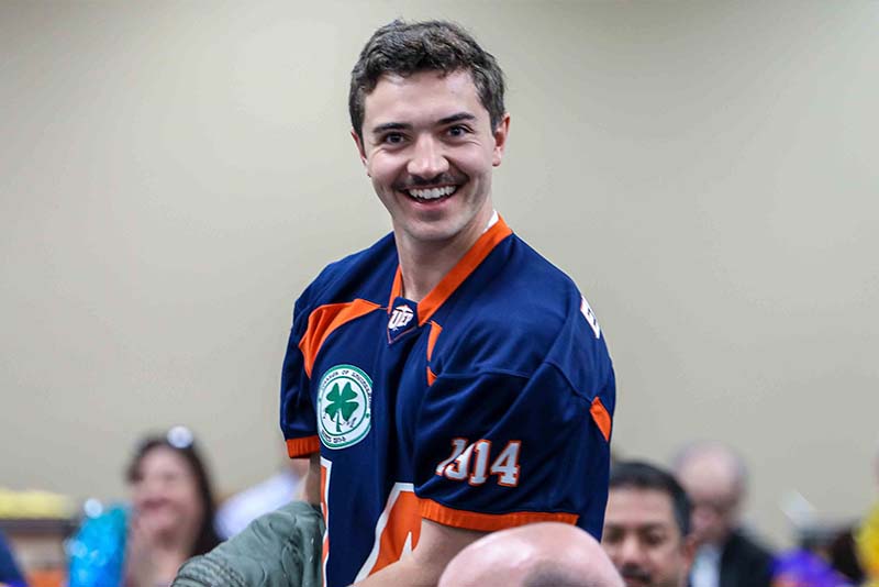 Person wearing a sports jersey standing among attendees at an indoor event.
