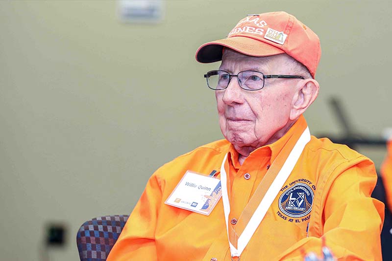 Willie Quinn wearing an orange shirt and cap seated at the Loya Engineering 2022 Homecoming breakfast.