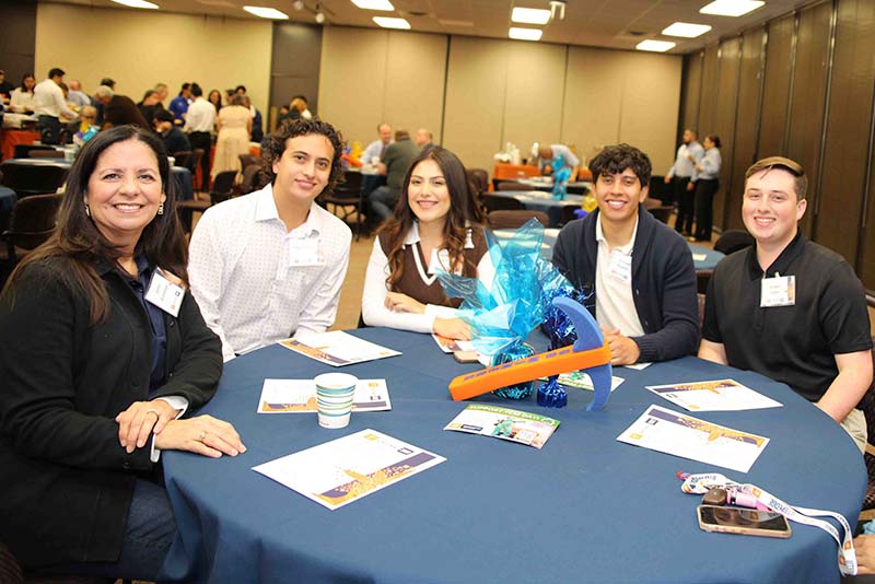 Five people seated around a round table during an indoor event.