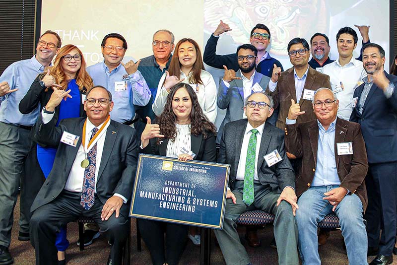 Group of people posing together with a Department of Mechanical Engineering sign in front of a projection screen.