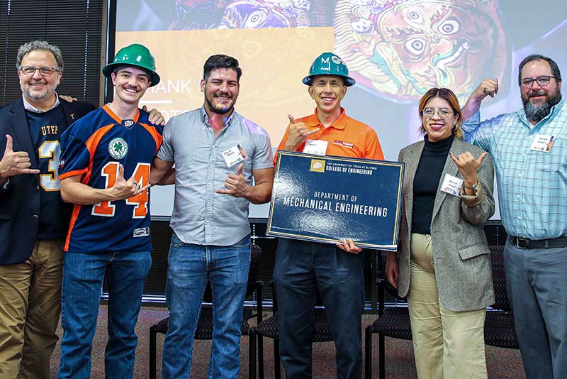 Group of people posing together with a Department of Industrial Manufacturing and Systems Engineering sign in front of a projection screen.