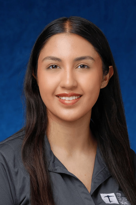 Professional headshot of Allie De La Riva wearing a gray button-down shirt with a UTEP College of Engineering logo, facing forward against a blue studio background.