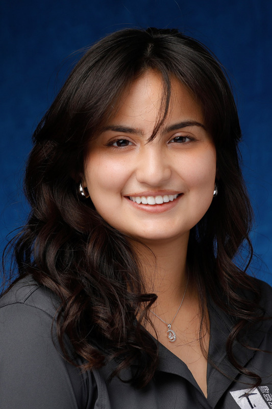 Professional headshot of Jocelyn Jimenez wearing a gray UTEP College of Engineering shirt, facing forward against a blue studio background with soft lighting.