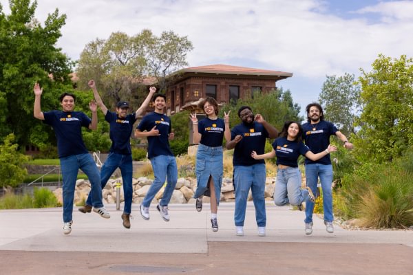 Mining Camp student leaders jumping together outdoors in front of a campus building.
