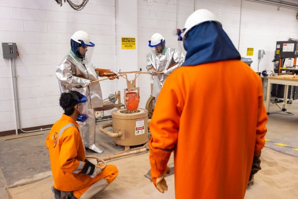 Mining Camp participants observing a foundry equipment demonstration in protective gear.