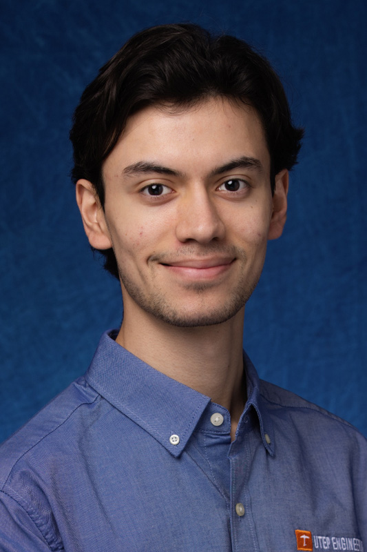 Professional headshot of Alejandro Payan wearing a blue button-down shirt with a UTEP Engineering logo, facing forward against a blue studio background.