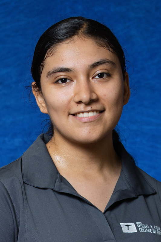 Professional headshot of Daniela Gutierrez with dark hair pulled back, wearing a gray UTEP College of Engineering polo shirt and facing forward against a blue studio background.