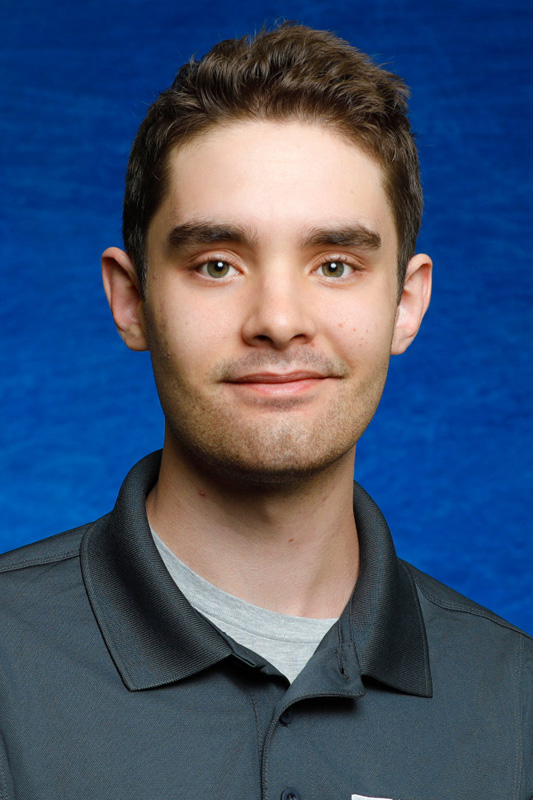 Professional headshot of Evan Espinoza with short dark hair wearing a gray UTEP College of Engineering polo shirt over a light-colored undershirt, facing forward against a blue studio background.