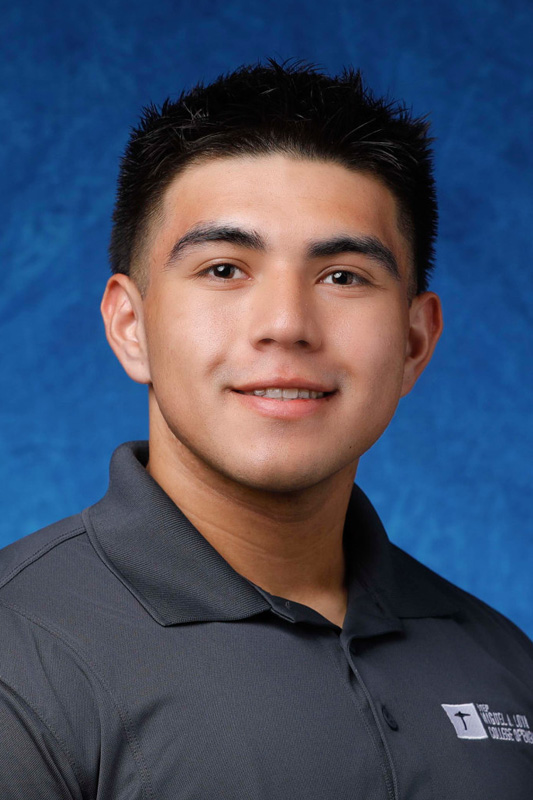 Professional headshot of Isaac Silva with short dark hair wearing a gray UTEP College of Engineering polo shirt, facing forward against a blue studio background.