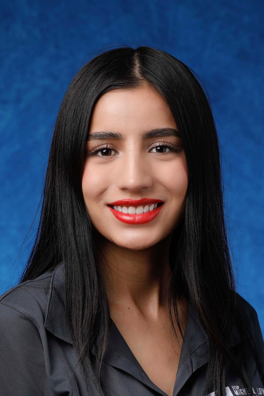 Professional headshot of Zayra Calvario with long dark hair wearing a dark crew-neck shirt, facing forward against a blue studio background.