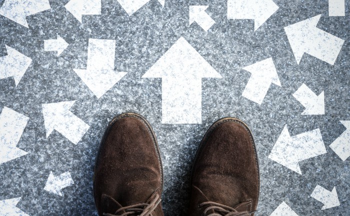 Man considering many options, standing on a road with many arrows