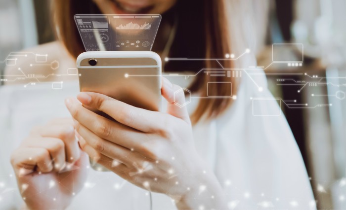 Woman using a smartphone that displays dashboards, social media, and interconnected electronic devices