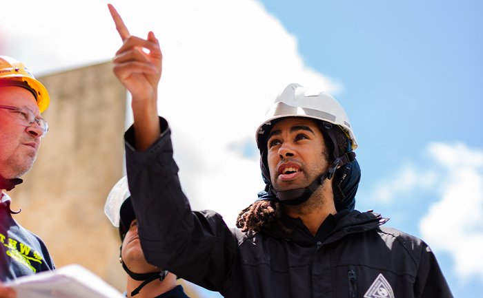 A man in a hard hat points out a structure to another man in a hard hat.