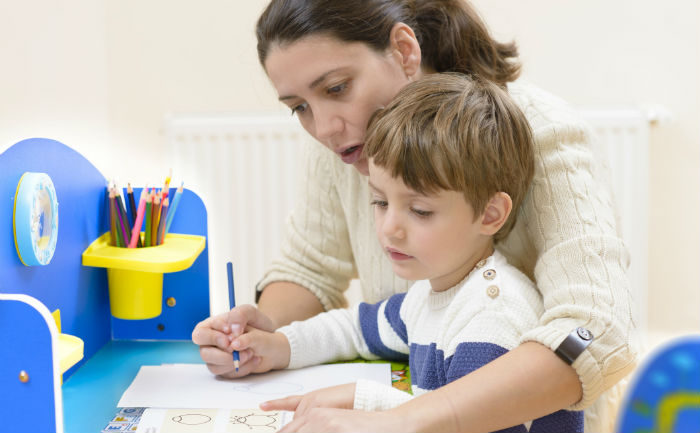 Woman teacher using her early intervention certification by working with a young boy on a coloring assignment.