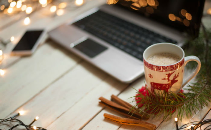 A laptop, phone, cup of cocoa, and cinnamon sticks sit on a table surrounded by strands of white Christmas lights as an example of one of the best and creative ways to study.