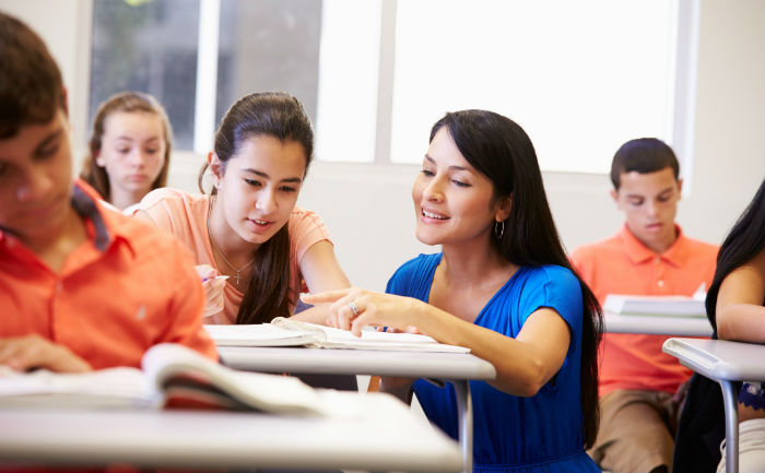 Hispanic woman putting her Master’s in Bilingual Education to practice by helping a young female student during class.