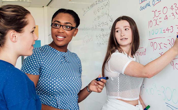 Teenagers asking for help from the teacher within mathematics class.