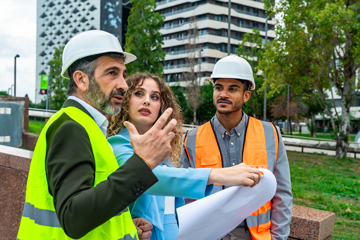Two men in hardhats and woman holding blueprints 