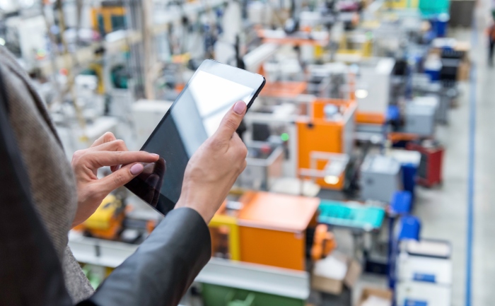 A business woman – a systems engineer – standing on a balcony, holding a tablet, and overseeing the functionality of a large manufacturing system. 