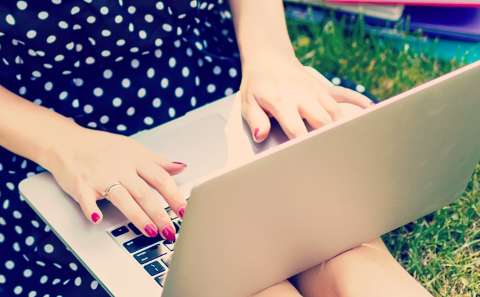 Woman studying outdoors on a sunny day, with laptop and notebooks by her side