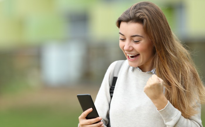 Excited female student reading news on her smartphone