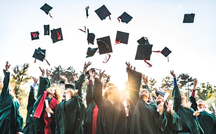 Illustration of graduate students welcomed by a teacher on the background of a planet, stacks of books, and laptops and tablets.