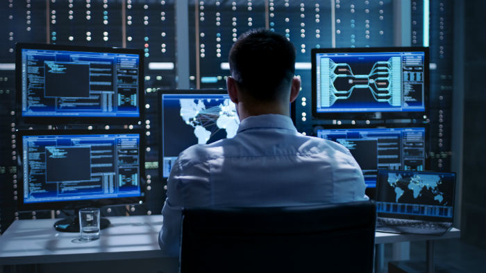 Man sitting in chair and working on several computer screens for a security studies job.