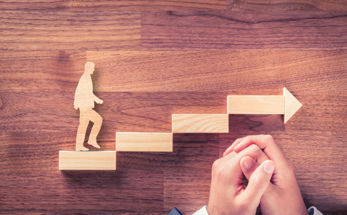 Wooden blocks stacked like a staircase with wooden man walking up them to represent career advancement.