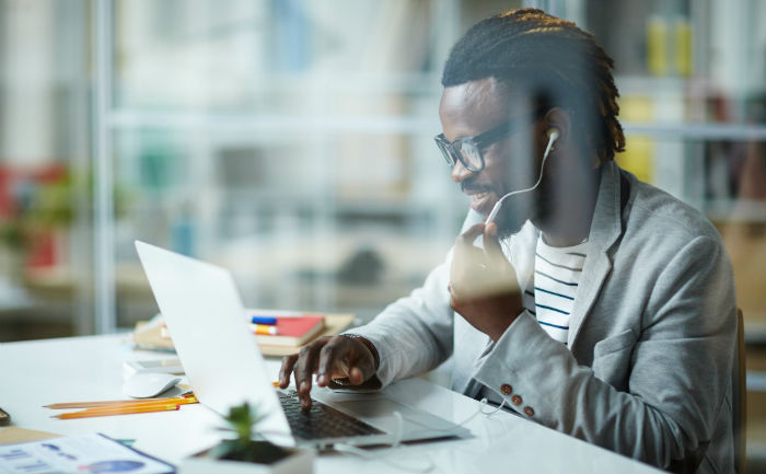 Man smiling and talking into headphones while working on laptop.