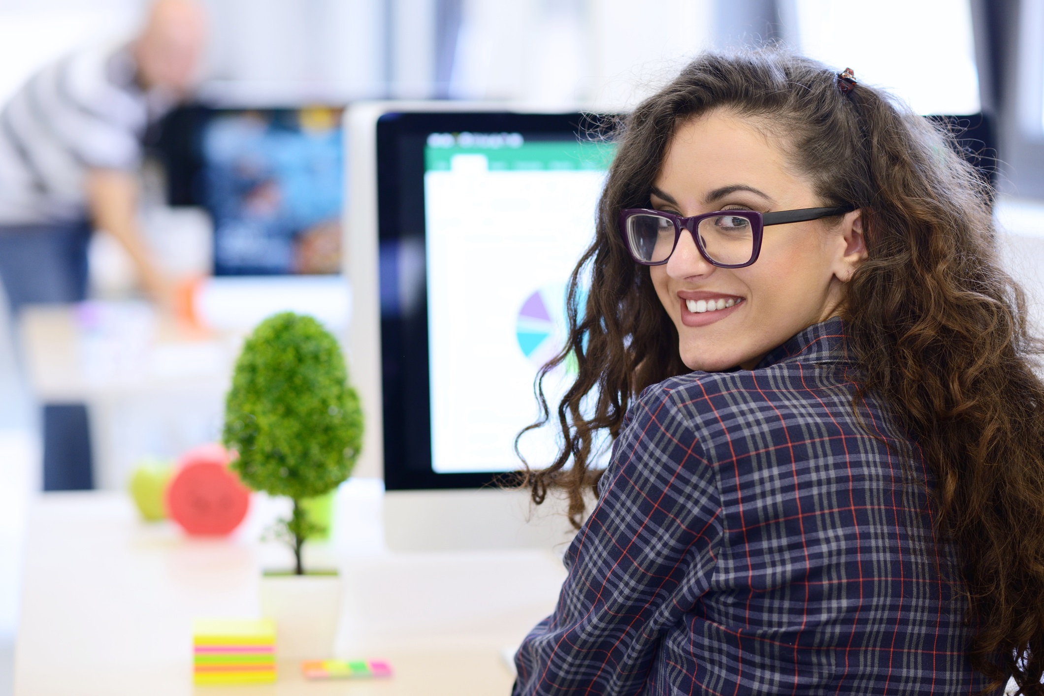 Smiling Hispanic woman sitting down with laptop in a room of people.