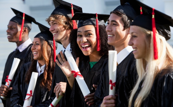 A group of young graduates in graduation gowns, smiling, holding their diplomas | UTEP Connect 