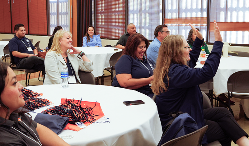 Utep faculty and staff engaging at a workshop with raised hands and happy faces