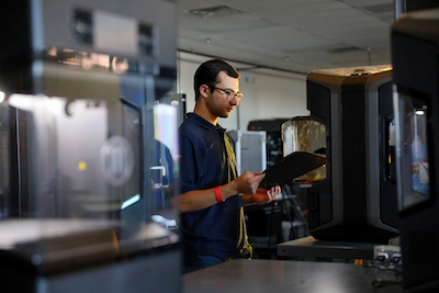 Photo Description” Luis De Leon, senior mechanical engineering major, checks inside a 3D printer in the 3D Engineering and Additive Manufacturing Technologies Center.