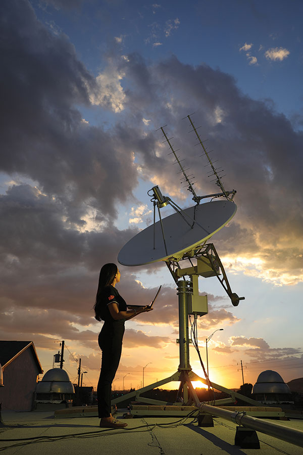 Andrea Vargas, a senior mechanical engineering major, stands next to a UHF/S-Band ground station tracking satellite array on the roof of the UTEP Aerospace Center's Spacecraft Design and Engineering Facility in El Paso. The array monitors satellite movements, including a small satellite that UTEP researchers helped construct and send into orbit in 2020. Photo: J.R. Hernandez / UTEP Marketing and Communications  