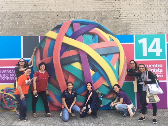 UTEP students and faculty, including Yvette Belinda Díaz and Associate Professor Eva Moya, Ph.D., (standing left, foreground), Julissa Corona and Patricia O. Carret (kneeling center) and Liliana Gomez (standing right, foreground) pose with other participants at the 14th Feminist Conference of Latin America and the Caribbean in Montevideo, Uruguay, in 2017. Photo courtesy of Eva Moya.  