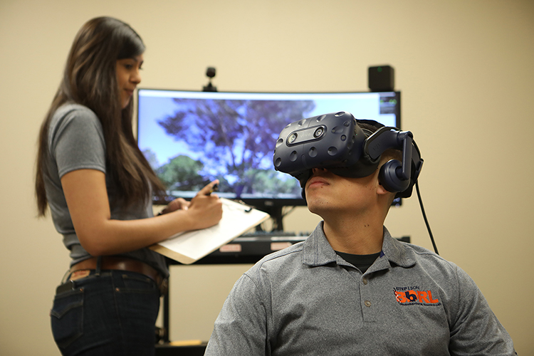 Ismael Beltran, foreground, wears a virtual reality headset as part of an immersive virtual reality study in UTEP’s School of Nursing. Project Manager Diana Flores, background, helps to conduct the study. Photo: J.R. Hernandez / UTEP Communications 